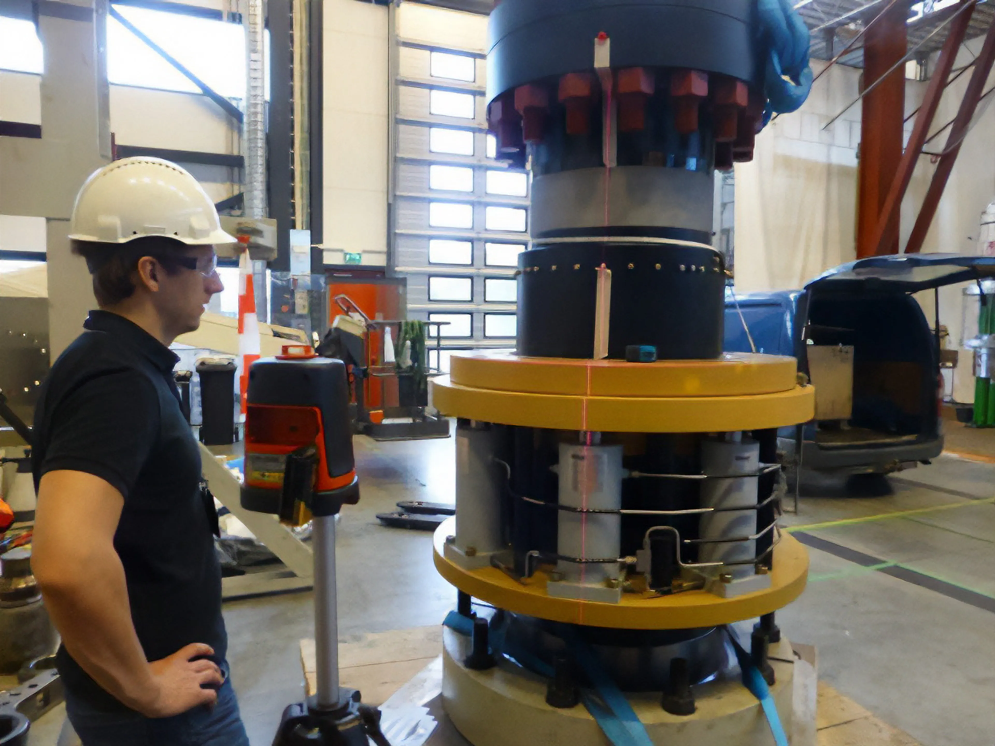Engineer standing next to a large cylindrical offshore component with mounted structural monitoring sensors during installation in an industrial test facility