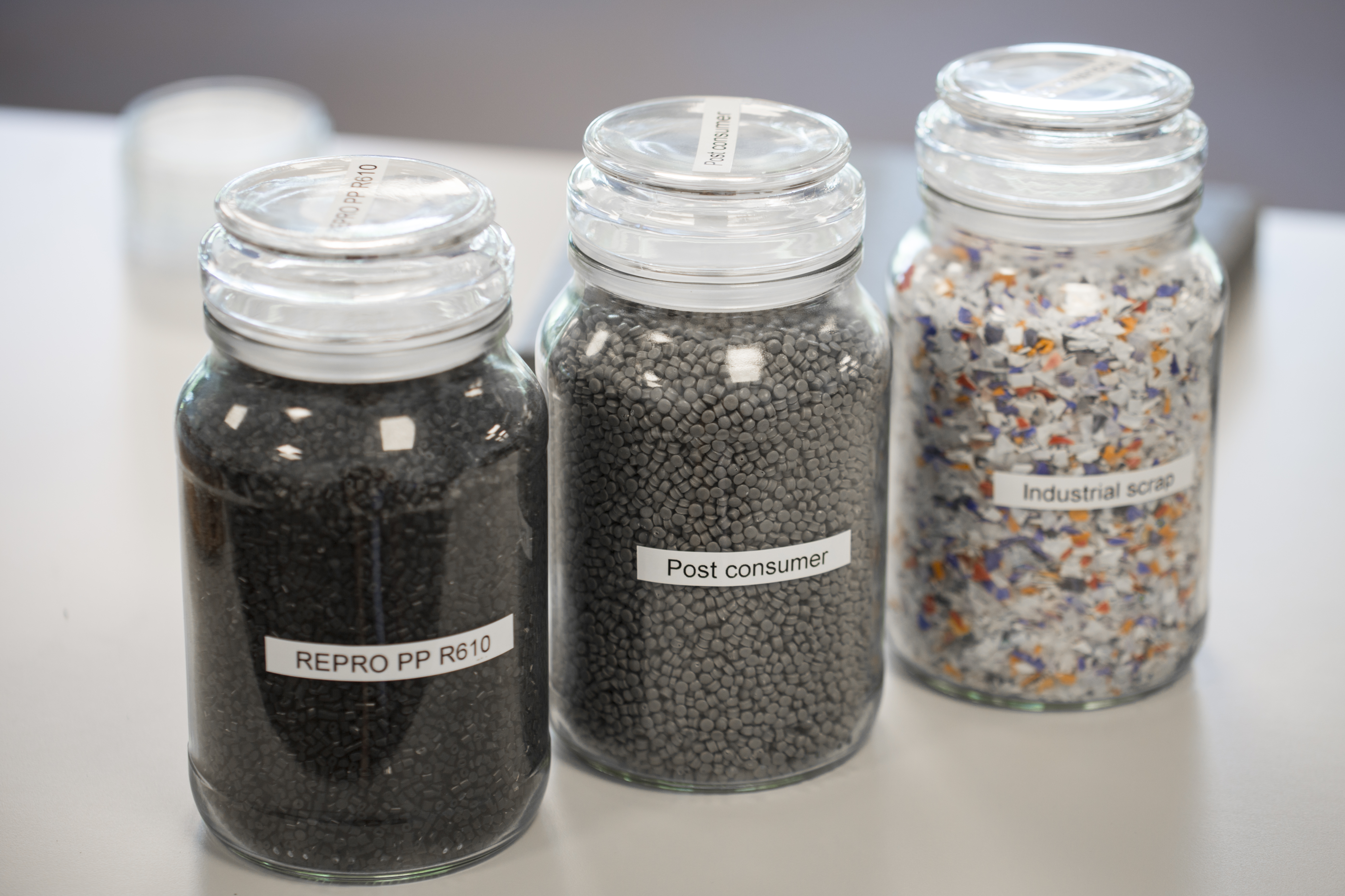 Three glass jars containing black, grey and mixed plastic granules for resource optimisation.