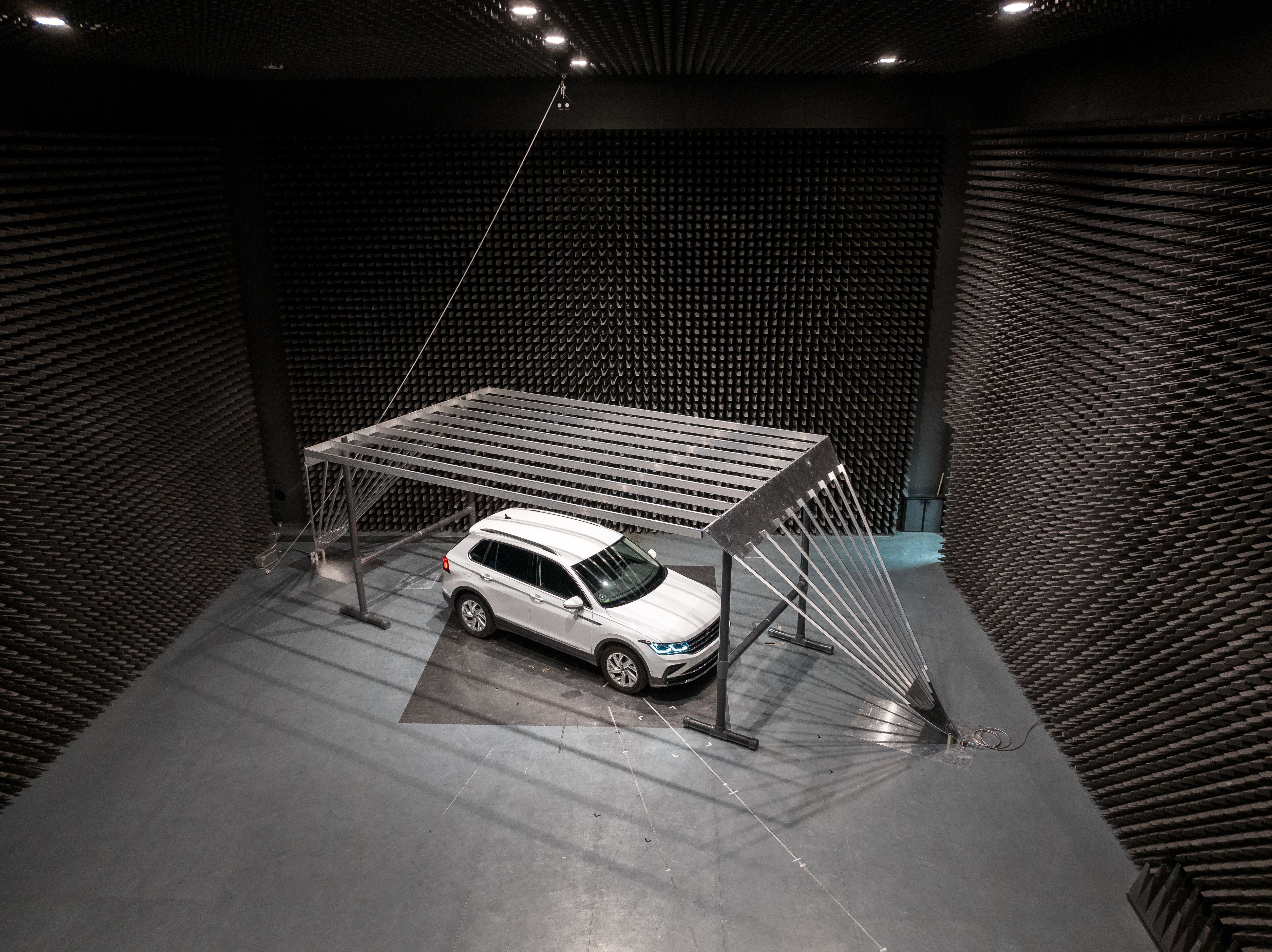 Semi-anechoic EMC testing chamber with absorber-lined walls and a vehicle positioned on a turntable.