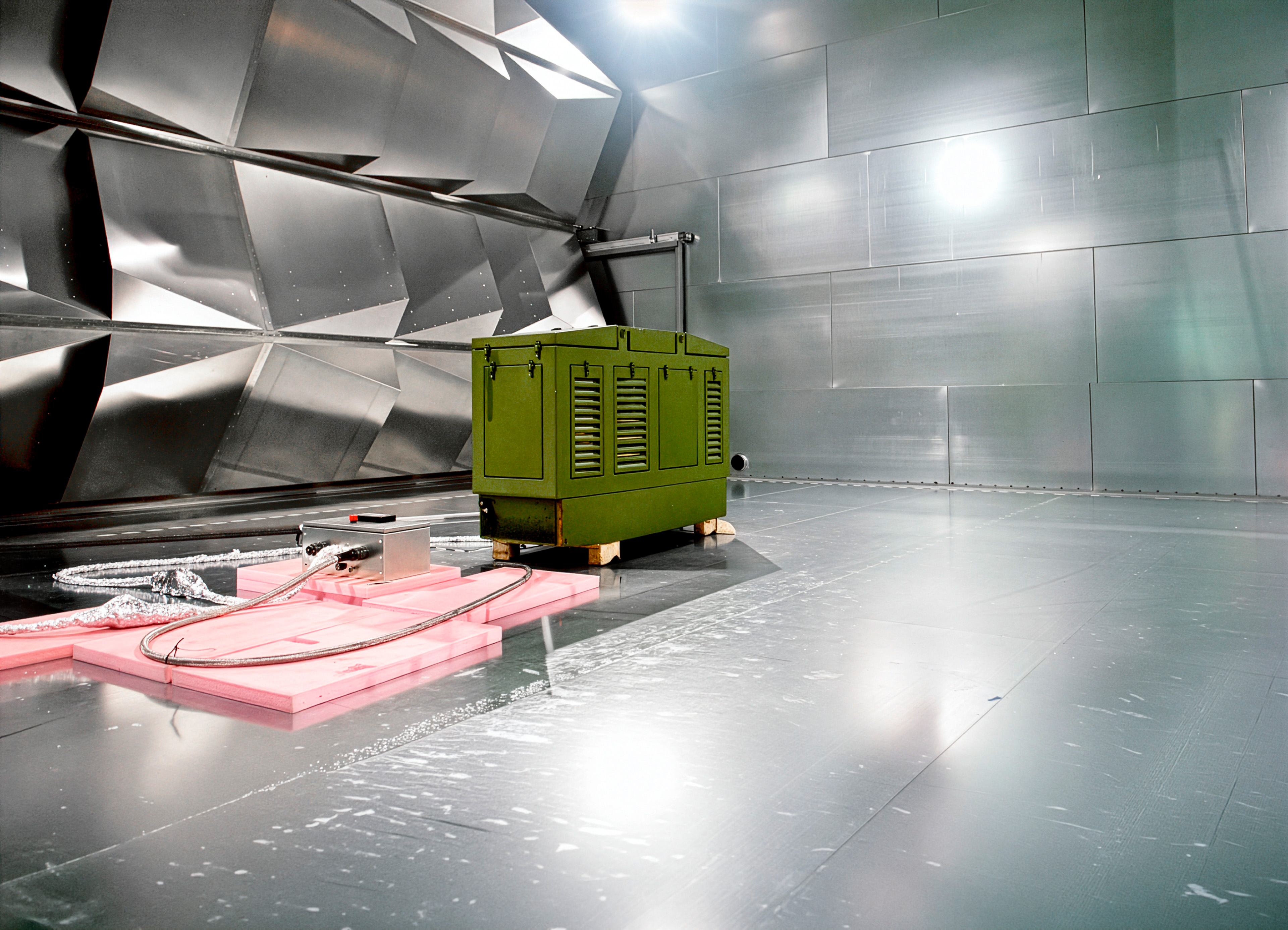 Stort metallisk reverberationskammer med reflekterende paneler og testudstyr placeret på gulvet til EMC-test.