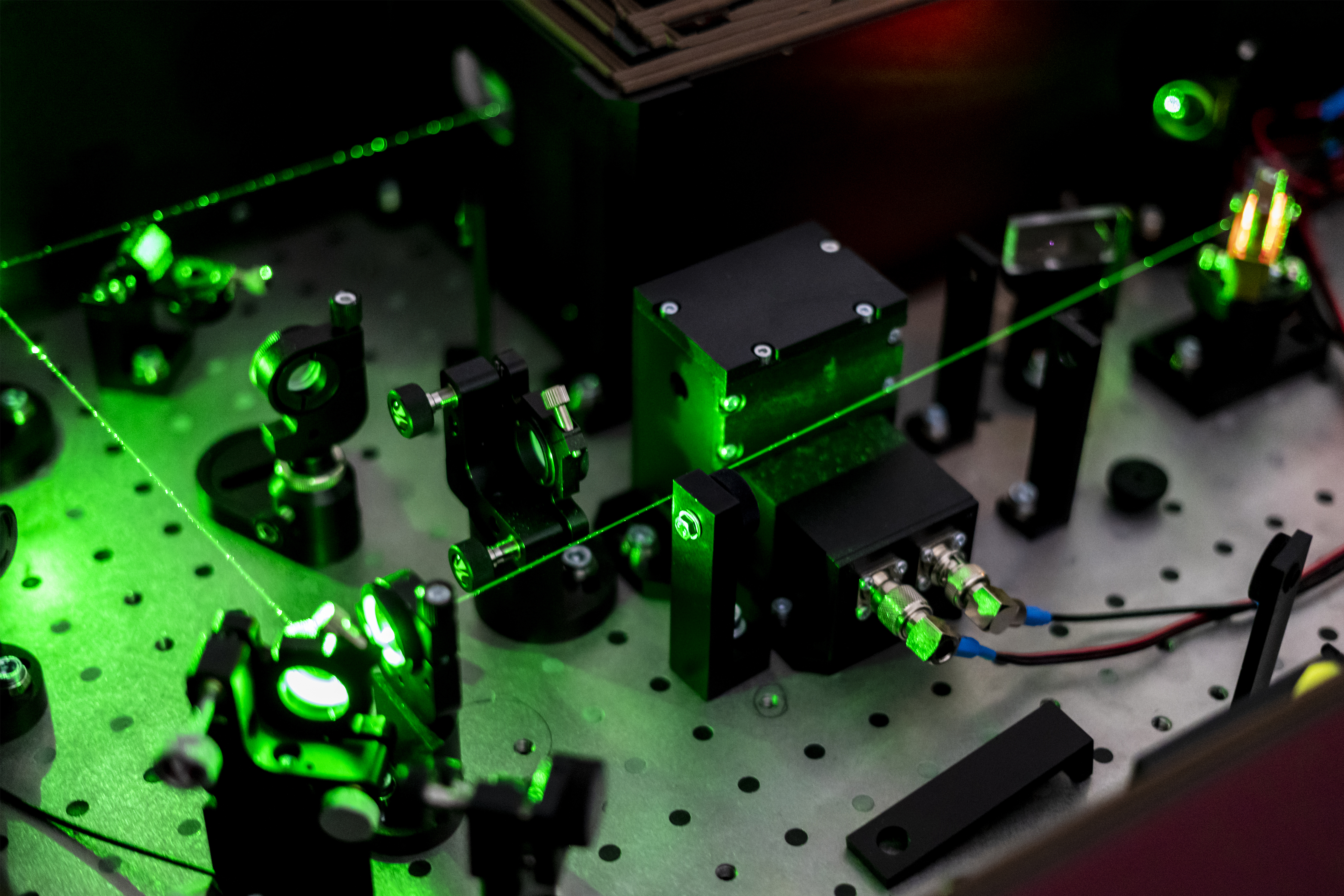 Optical laboratory setup with green laser light passing through lenses, mirrors and mounted photonics components.