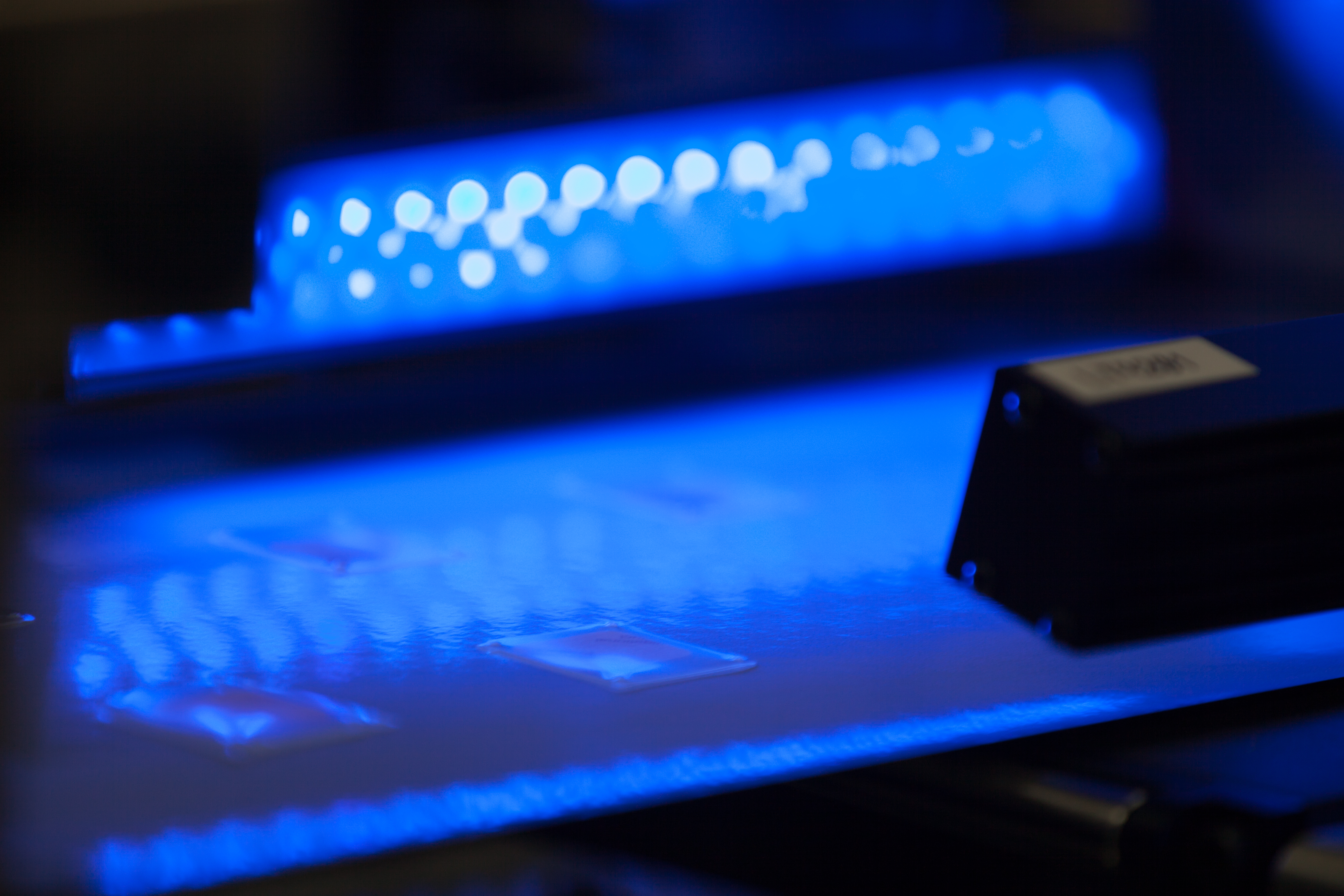 Close-up of photobiological lighting testing setup with blue illuminated light source and measurement sensor in a dark laboratory environment.