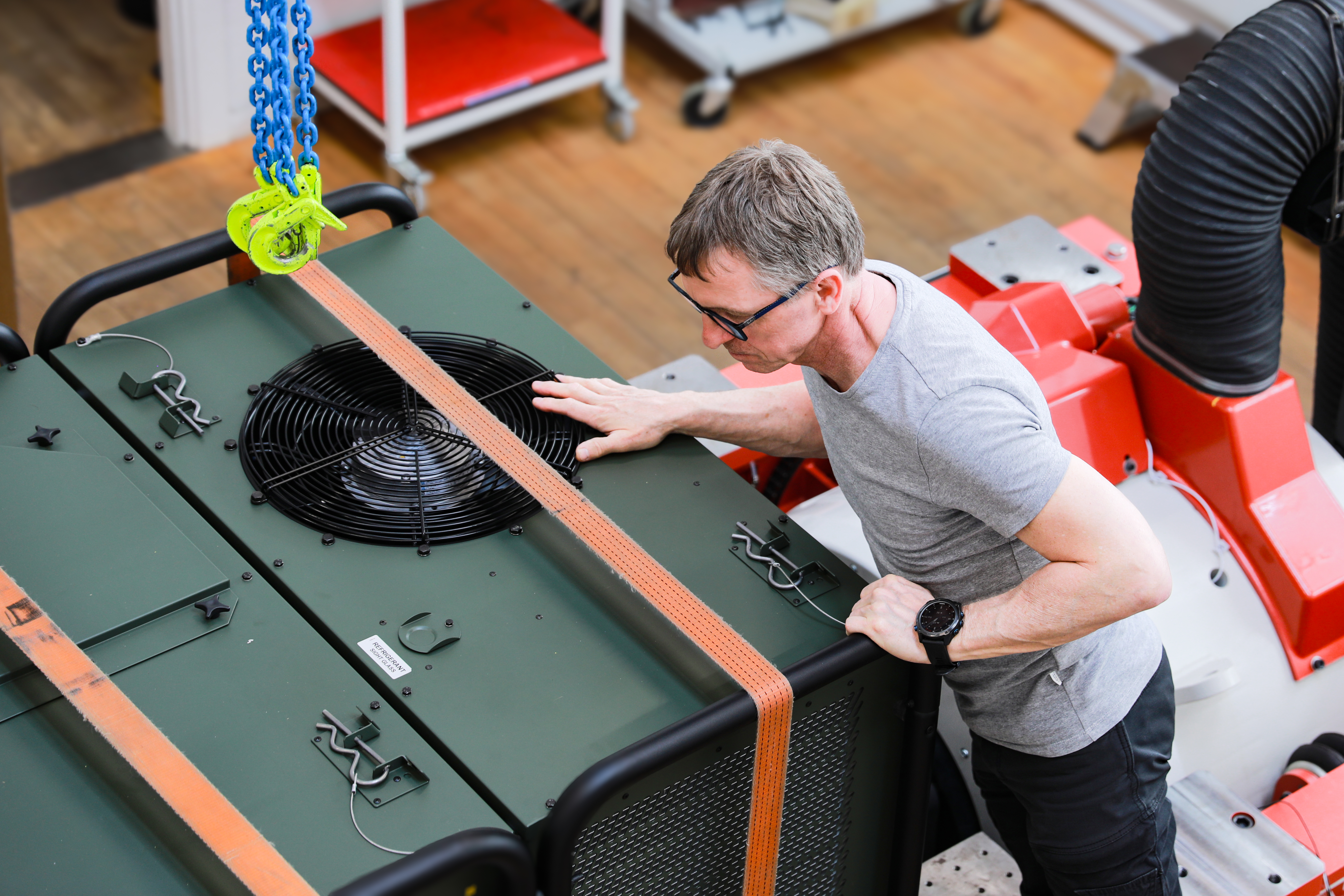 Test personnel inspecting equipment used for mechanical testing of products and components, including a secured unit with lifting straps, in a laboratory environment.