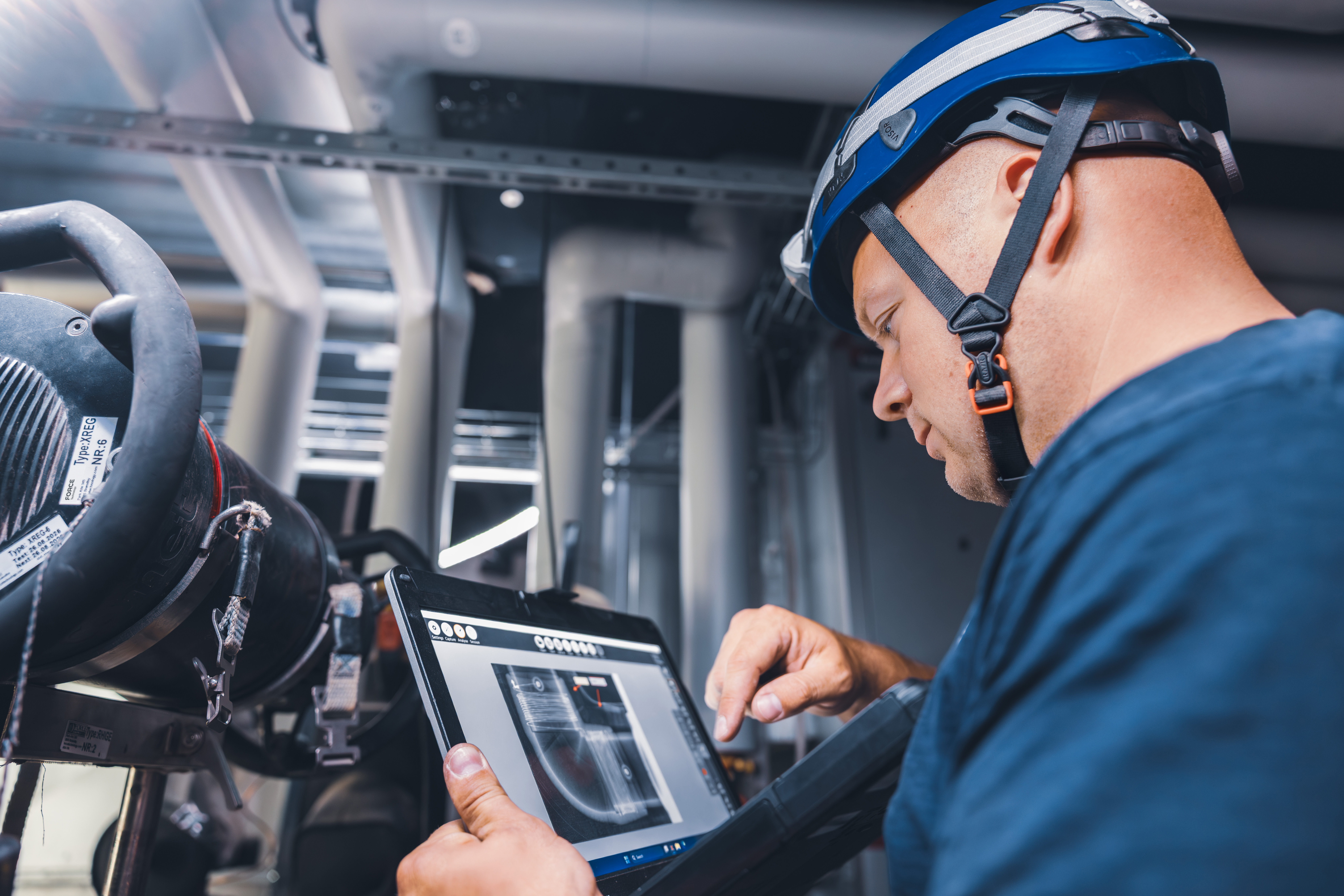 Tekniker bruger en tablet under NDT-inspektion af industrielle rørsystemer i et procesanlæg.