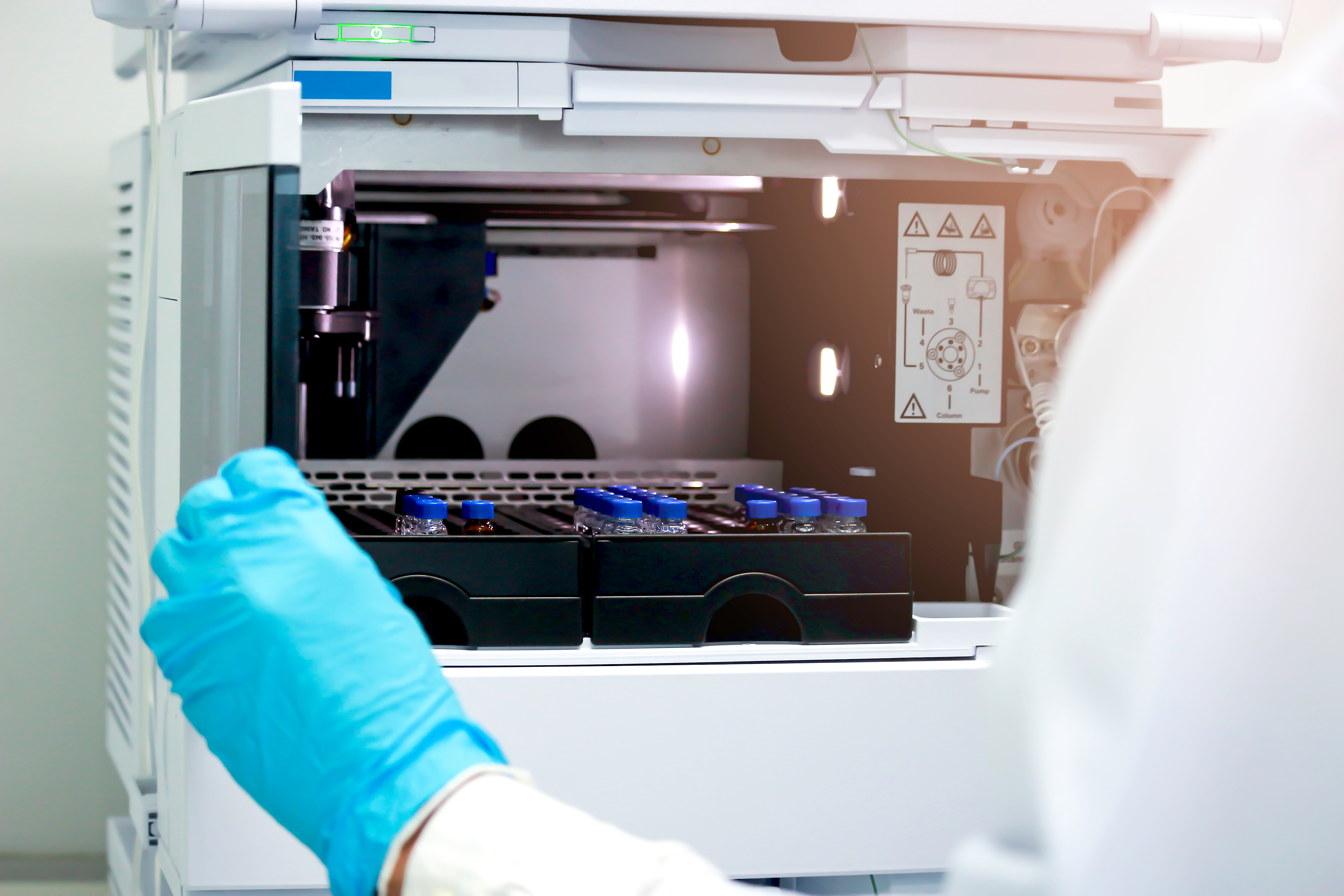 Gloved laboratory technician placing small sample vials into an analytical instrument.