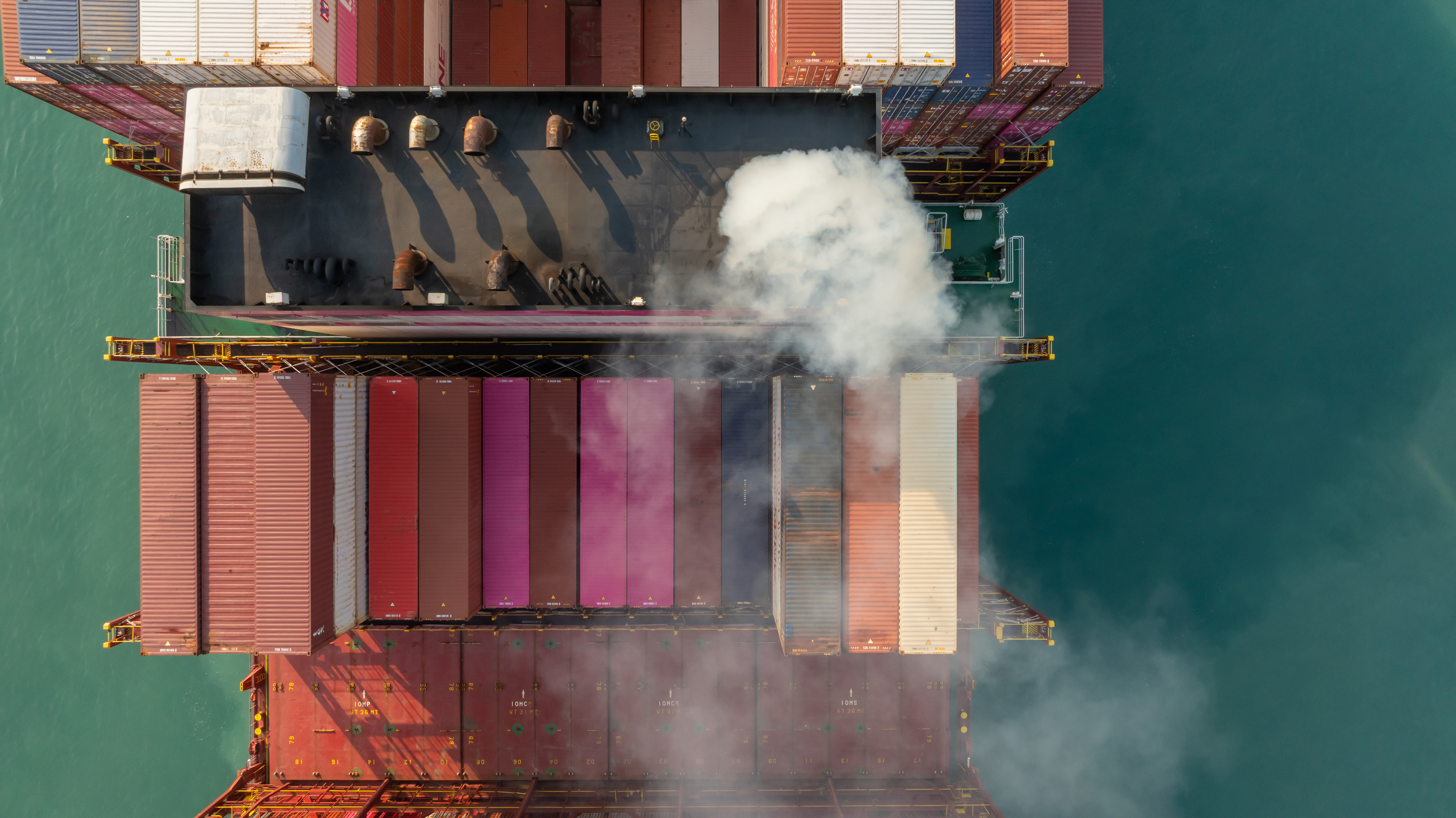 Et containerskib til søs med synlige udstødningsemissioner mellem stablede containere.